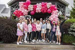 A group of smiling golfers stand infront of a baloon arch