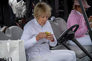 A woman wear white eats a wrap in a golf cart