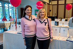 Two women wearing pink sweaters with the letter T pinted on the sweaters pose smiling for a photo