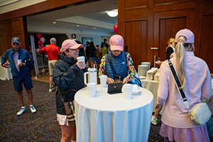 Three women wearing pink hats laughing while drinking coffee