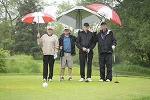 Four golfers pose for a picture holding umbrellas