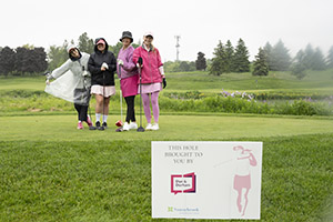 Four golfers smile in the rain in front of a Sunnybrook golf sign