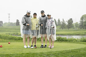 Four golfers wearing rain jackets stand side by side for a photo
