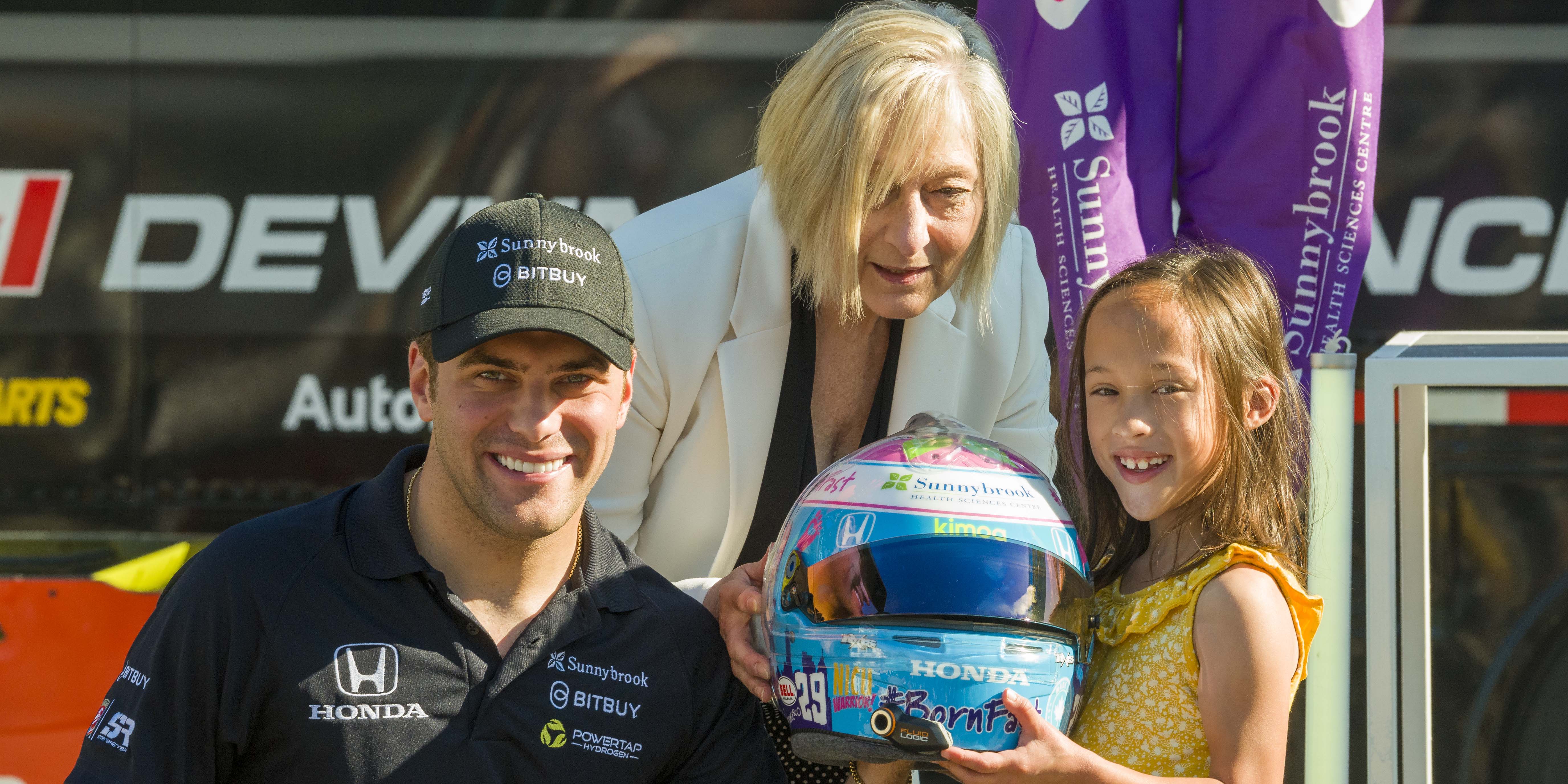 A man, woman and child pose for a photo holding a racing helmet