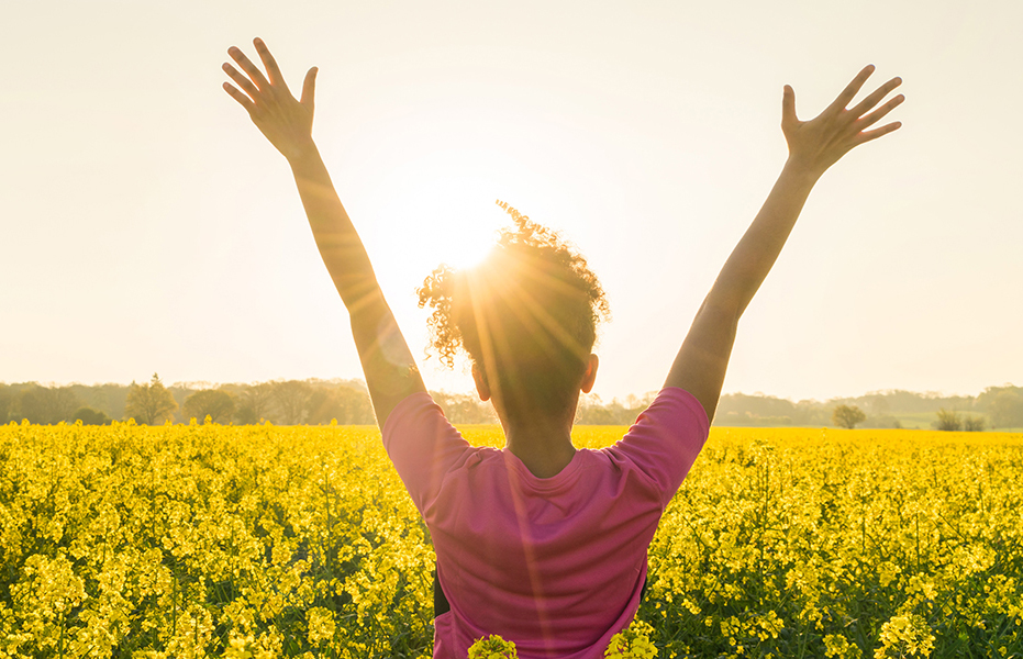 A woman holds her hands up to the sky in a field