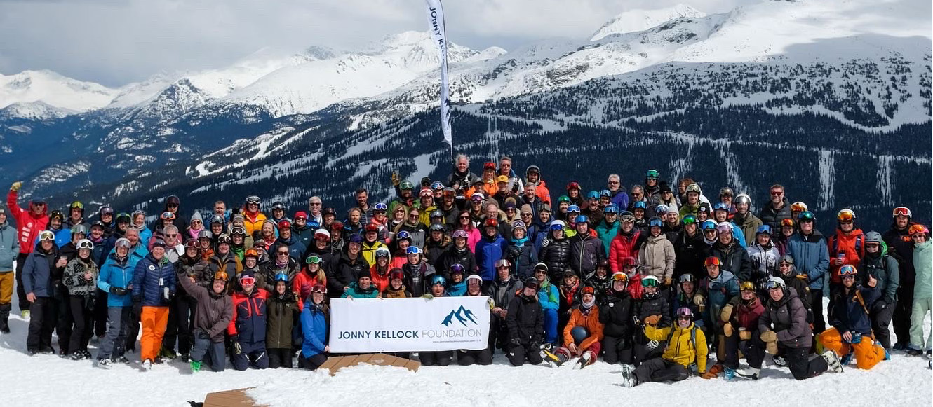 A large group of skiers gather atop a mountain