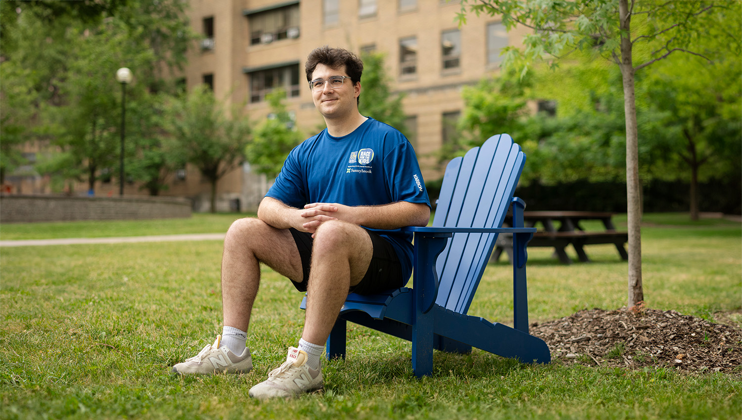 Jonathan sits in a chair outside of Sunnybrook hospital wearing a RBC race for the kids t-shirt