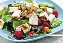 A picture of a healthy salad with chicken, raspberries, tomato and spinach. .