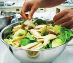 A person puts slices of pear on top of a salad with romaine lettuce.