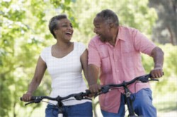 A smiling, older couple bikes on a wooded trail.