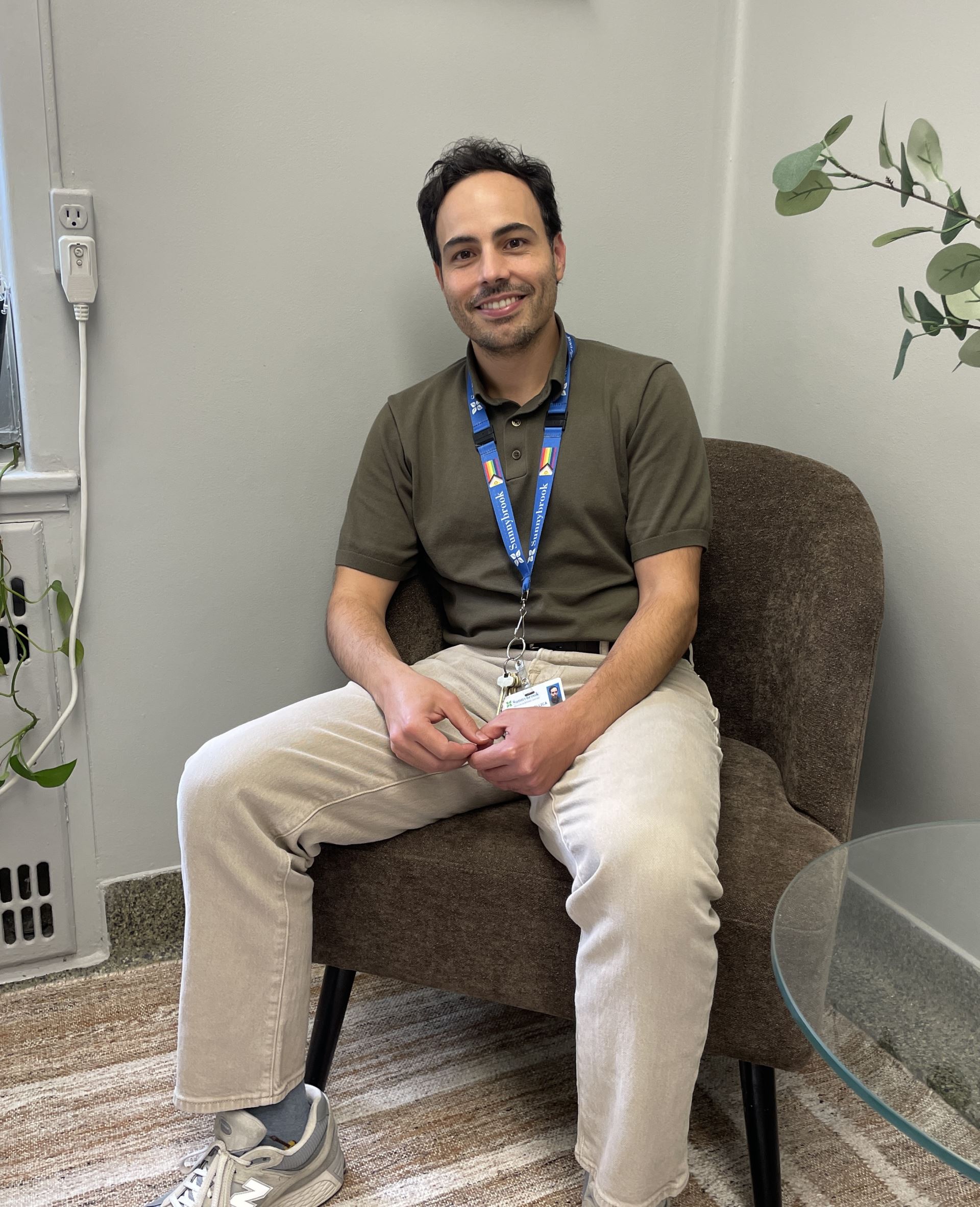 A man wearing a green shirt and khaki pants sits in a chair in a medical office.