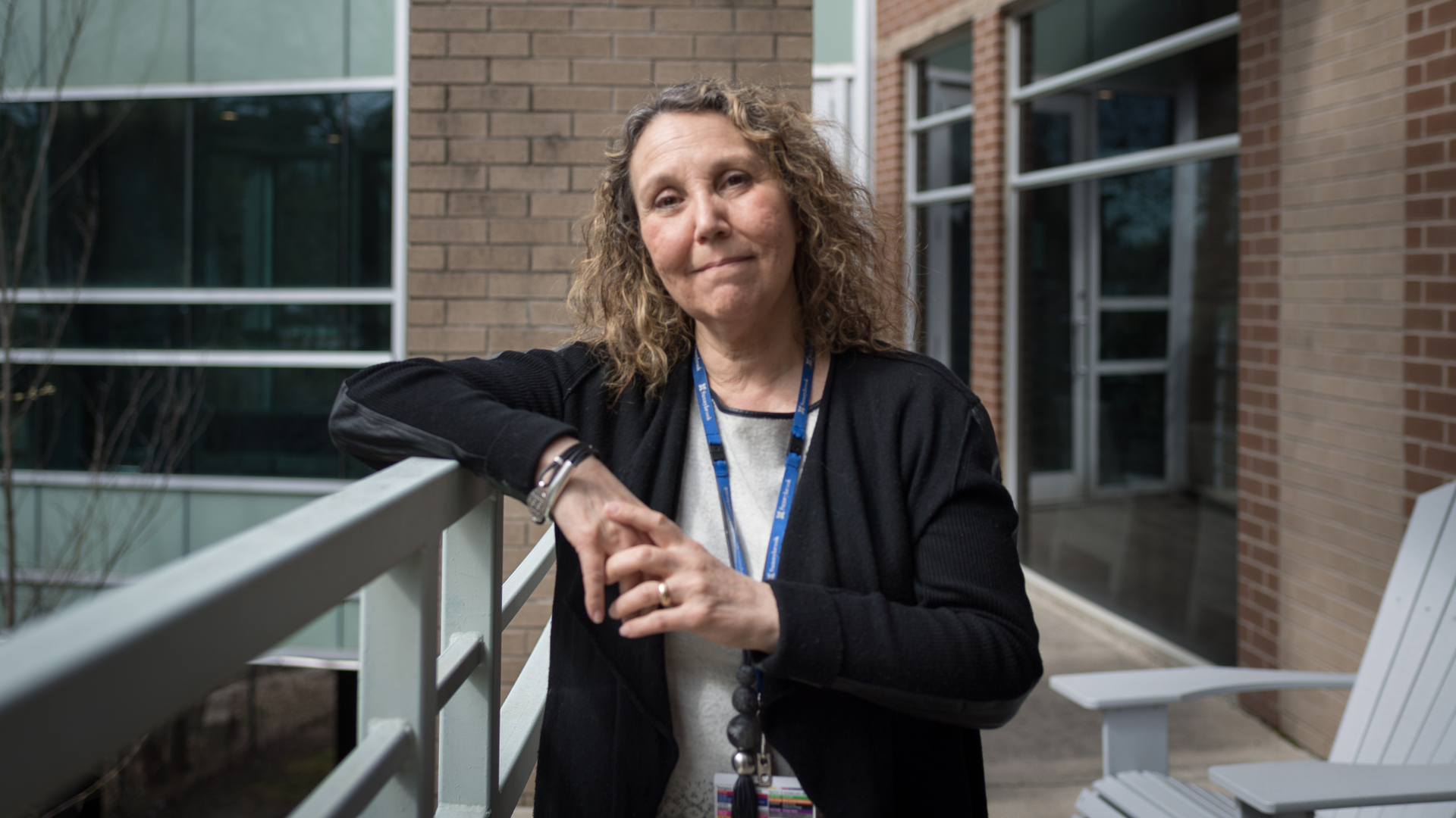 A woman with curly hair stands on a balcony with her elbow resting on the ledge
