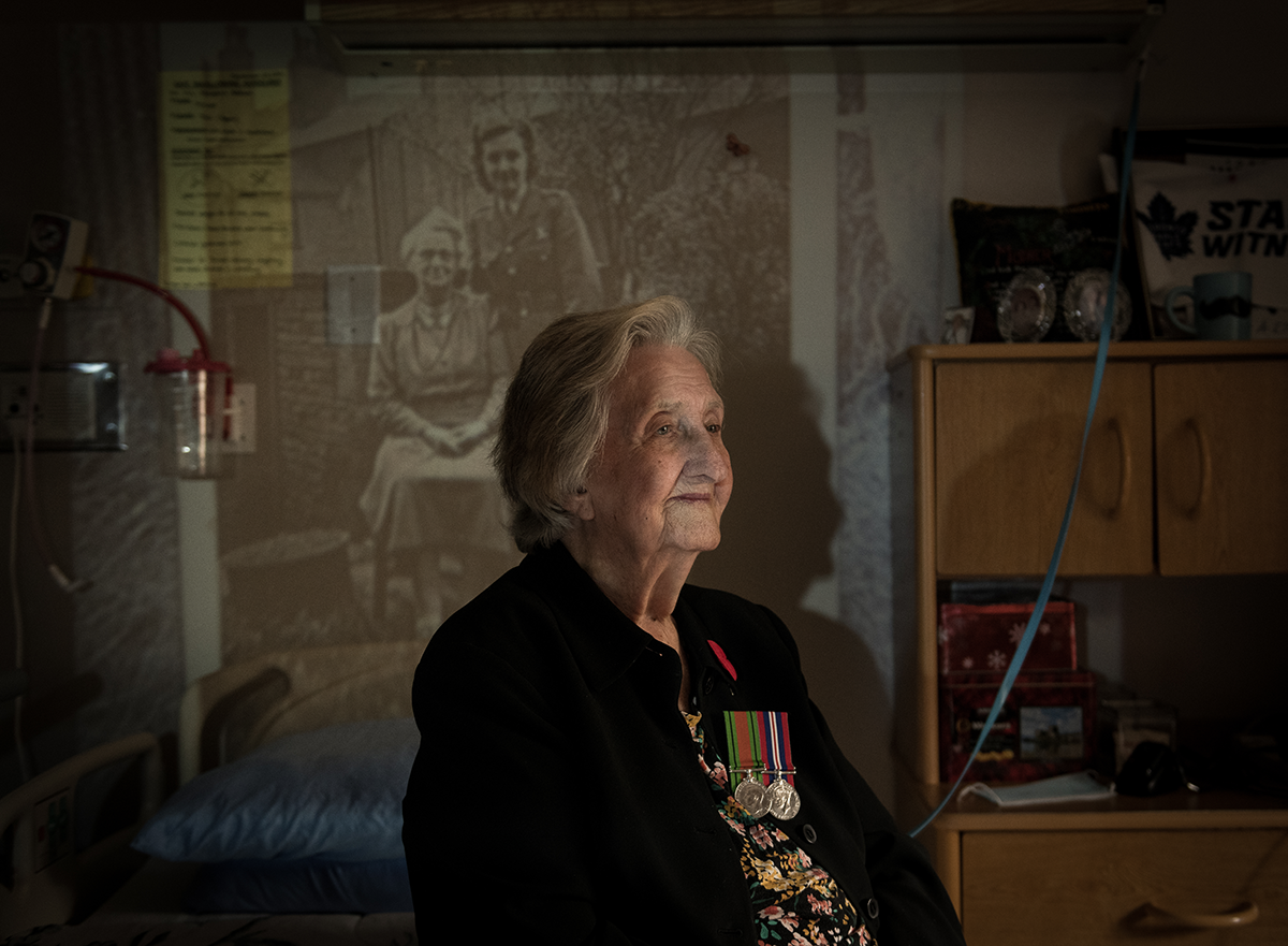 Margaret Addison, pictured wearing her medals. She sits in front of a projected image of herself during the war. 
