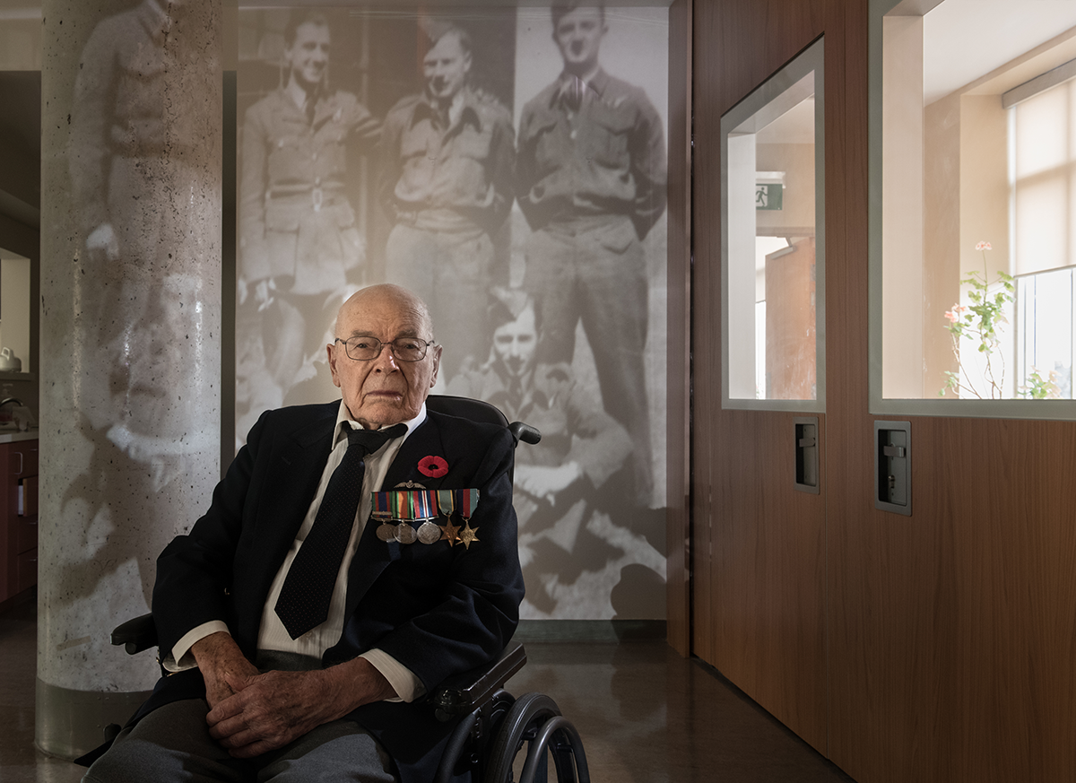 Ken Hawthorn sits pictured in front of an image of himself and others during the war 
