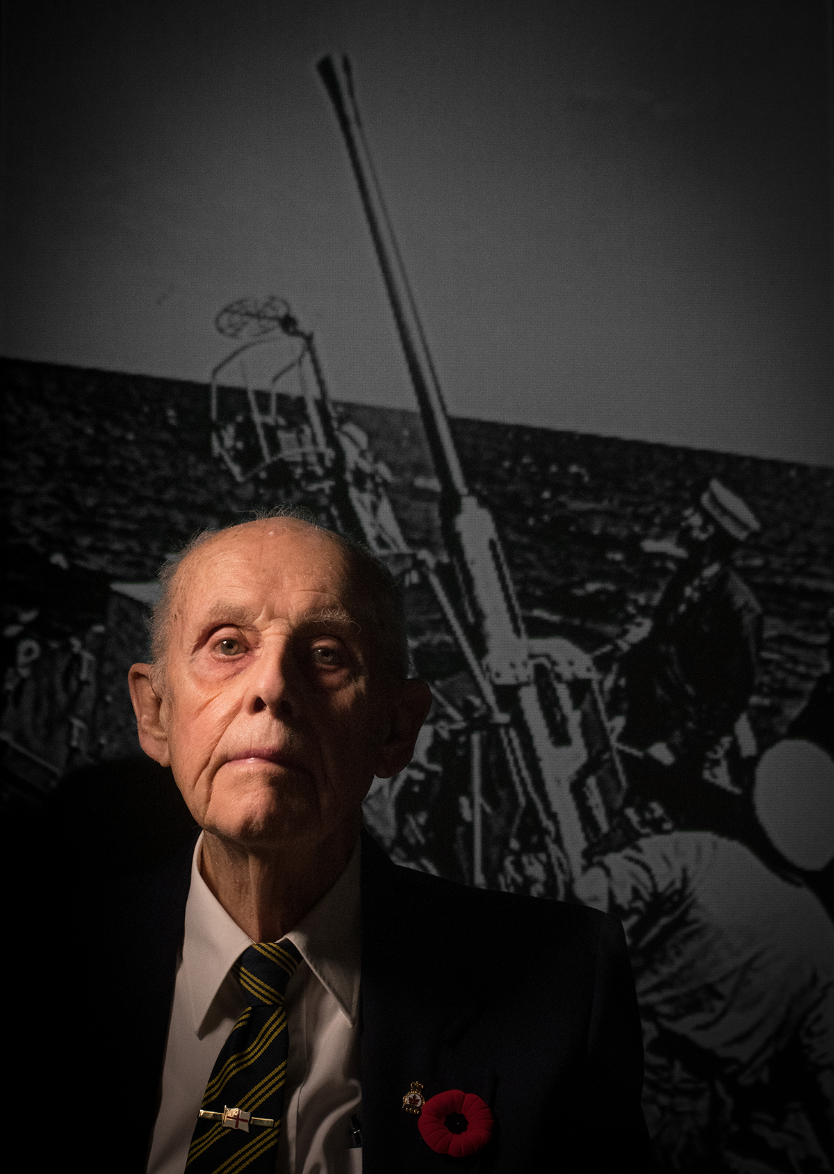 Jim Lister is photographed in front of an image of himself taken during the war times.