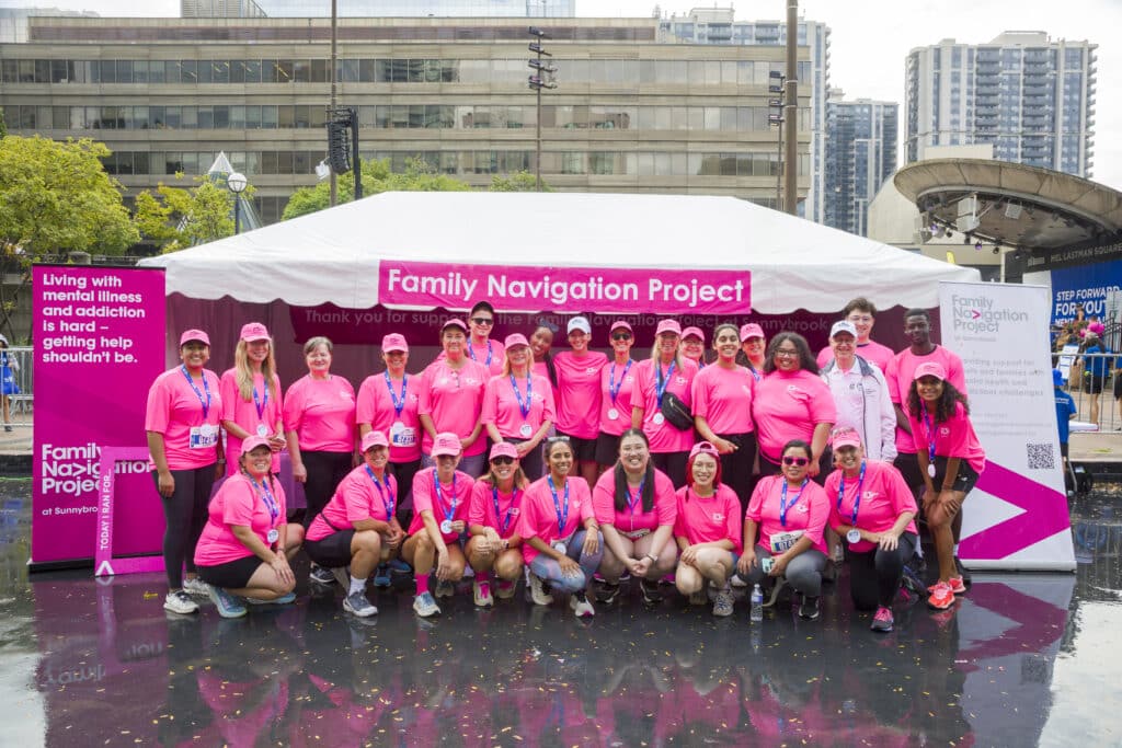 A large group of people wearing bright pink shirts stand outside in front of an event tent at the RBC Race for the Kids.