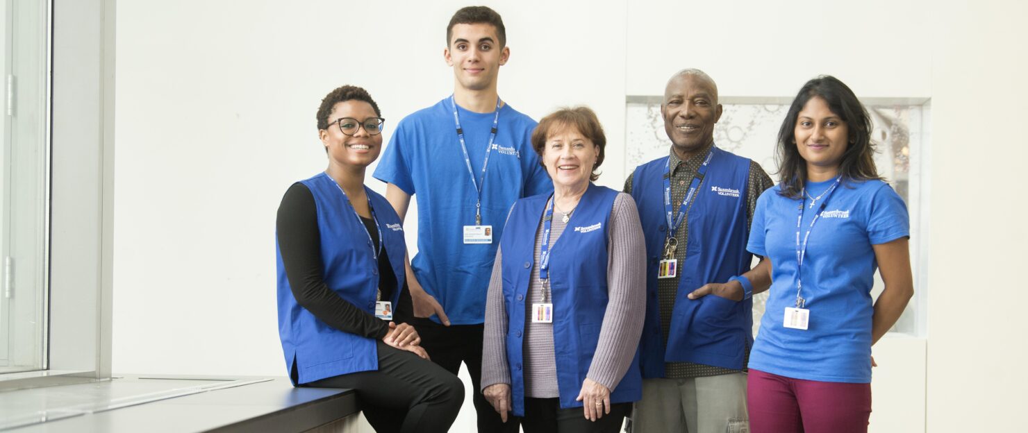 Five volunteers posing in the hospital wearing their blue Sunnybrook volunteer uniforms.