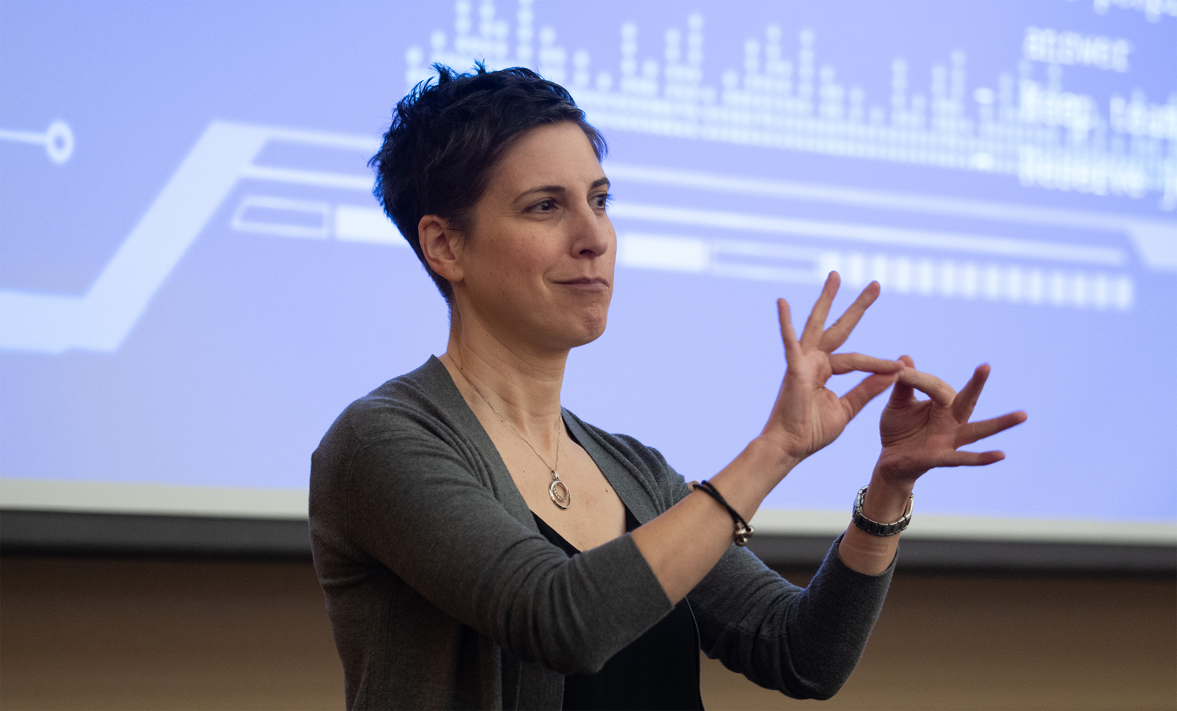A person with short dark hair signs using her hands in front of a blue screen.